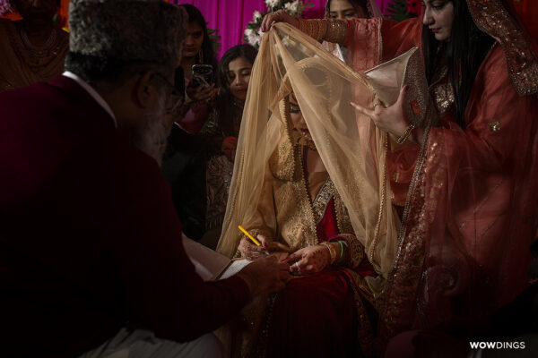 muslim bride lifting veil to sign nikaahnama marriage contract at a wedding in delhi