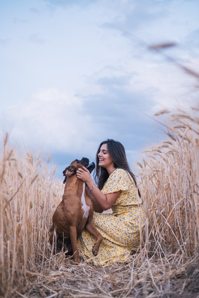 Portrait of a young woman hugging her dog in the middle of a wheat field.